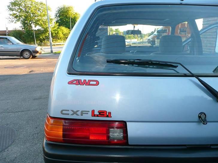 Daihatsu Charade Udstyr og Varianter - Sådan ser type skiltet ud standart på en 4WD model.

Mange har spurgt til hvorfor der er sat et 4WD skilt på, men sådan ser det altså ud standart og der er mange som skal have det bekraftet ved at lægge sig ned på alle 4 for at se om der nu også virkelig sidder et bagtøj samt trækaxler ud til baghjulene :o)

Det er bestemt ikke hverdag man ser en Charade med Full Time 4WD i DK
Det er der heller ikke noget underligt i da den model aldrig er solgt på det danske marked.
Og efter sigende skulle der kun være 7 importerede hvoraf de 4 er afgået ved døden og enten fortsat liven hos en hugger eller bil pressen hos skrot handleren.
Så hele 3 inkl min skulle der være i DK med plader på. (det kalder jeg en sjælden model) :o)

Man ser også en af model forskællighedderne ved baglygterne da nogle er leveret med et rippede lygteglas som på billedet og andre som oftest nyere end 93 modeller er leveret med et helt glat lygteglas. billede 11