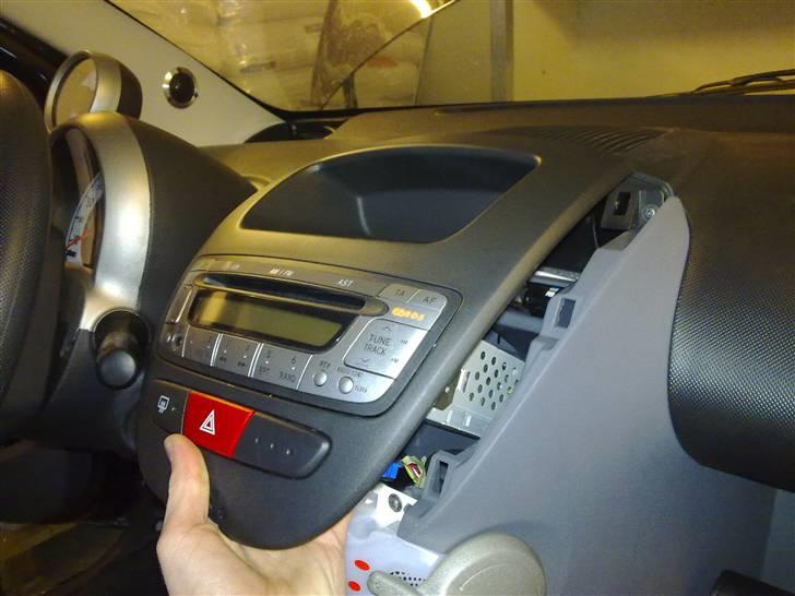 Sådan afmonteres radio i Aygo - Rammen sidder godt fast med plastikklips rundt i kanten, du kan løsne dem forsigtigt med en skruetrækker, det er nemmest at starte nederst i en af siderne.
Igen hvis du har en plastik spartel eller ligende er det bedre end en skruetrækker. billede 3