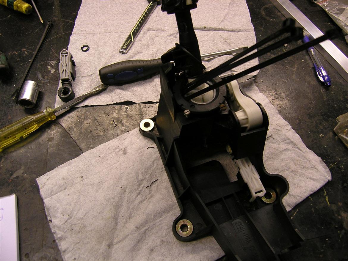 Gearstangsslør - tag en lille skruetrekker og lav plads mellem bosning og den sorte ring ikke ind til den vide kugle men udenfor og put stripsene ned imellem, rigelig langt ned til der ikke er mere slor, og derefter klip dem af billede 4