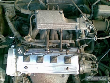 Toyota Carina E St. Car - her et billed af motoren.. som man kan se på indsugningssiden går der to rør til hver cylinder. betyder det er en lean burn. billede 10