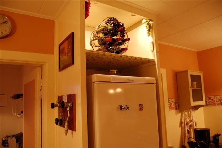 Landkøkkenet får en tiltrængt forandring - Skabet over køleskabet mistede sin låge og blev til vinskab med indbyggede spots. Her er en fin temperatur til vinen, men den er svær at nå. Uret til venstre er fra 4oèrne og drives af lysnettet. billede 9