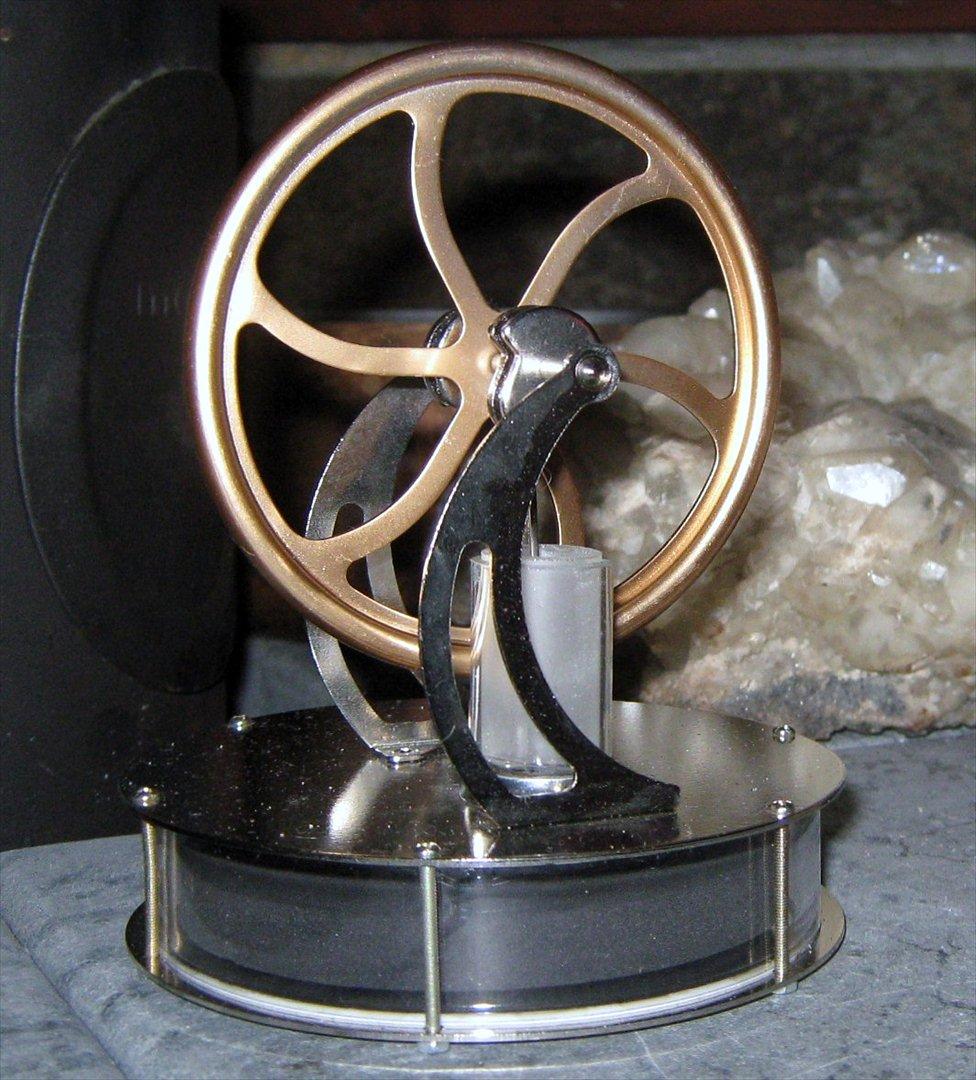 Stirling Motor - En "Stirling motor" er en motor som omdanner varme-energi (temperaturforskel) til bevægelse. Ved at der er en temperaturforskel på omkring 20 grader celsius (eller mere) imellem motorens overside og underside, vil hjulet begynde at køre rundt.

Denne Stirling motor kan for eksempel placeres ovenpå på et elektrisk apparat, radiator eller et stearinlys (et stykke væk fra), hvorved den efter et kort stykke tid vil kunne begynde at køre. Den kan ligefrem køre på is!

Denne motor vil begynde at køre ved en temperaturforskel på 20 grader celsius, hvor det højeste antal omdrejninger i minuttet den kan foretage er 180-200 (RPM).

Den er bygget i stål og glas. Den er 12 cm bred, 15 cm høj og vejer 250g.  billede 1